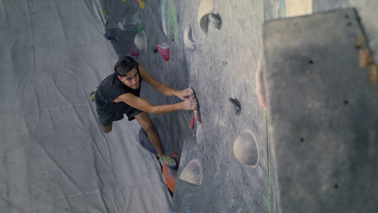 A climber gripping holds on a bouldering wall, seen from above