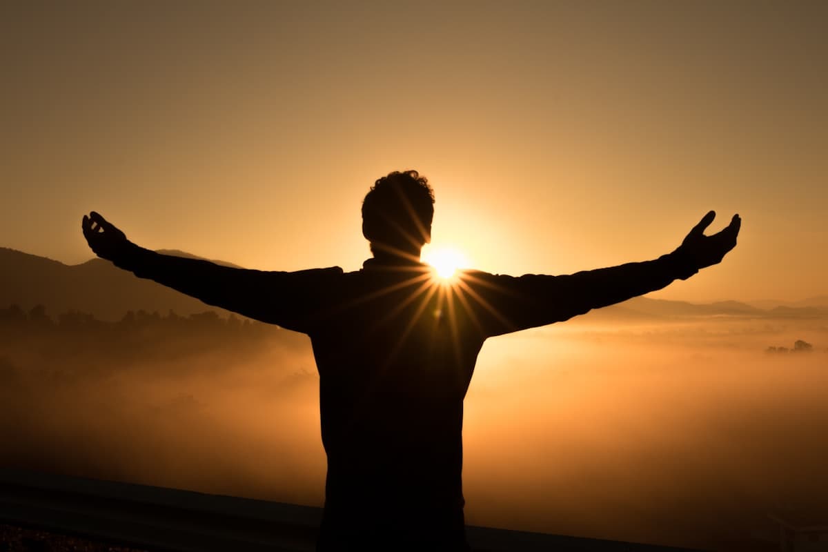A person with arms opened wide to the sunrise
