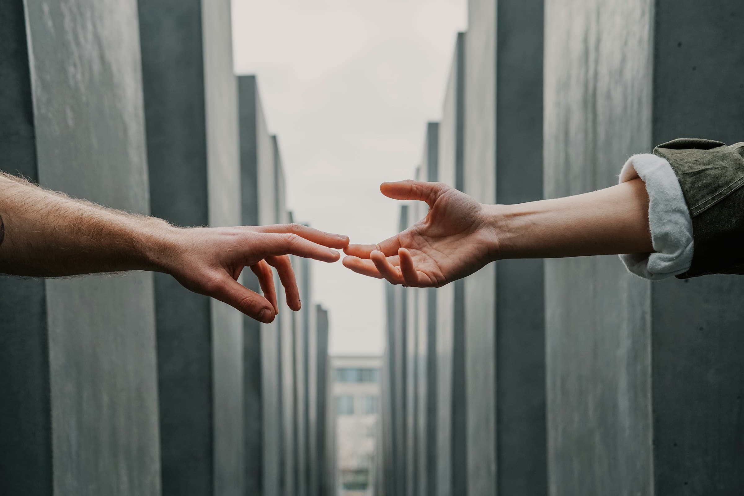 Two hands reaching toward each other across a gap between concrete walls