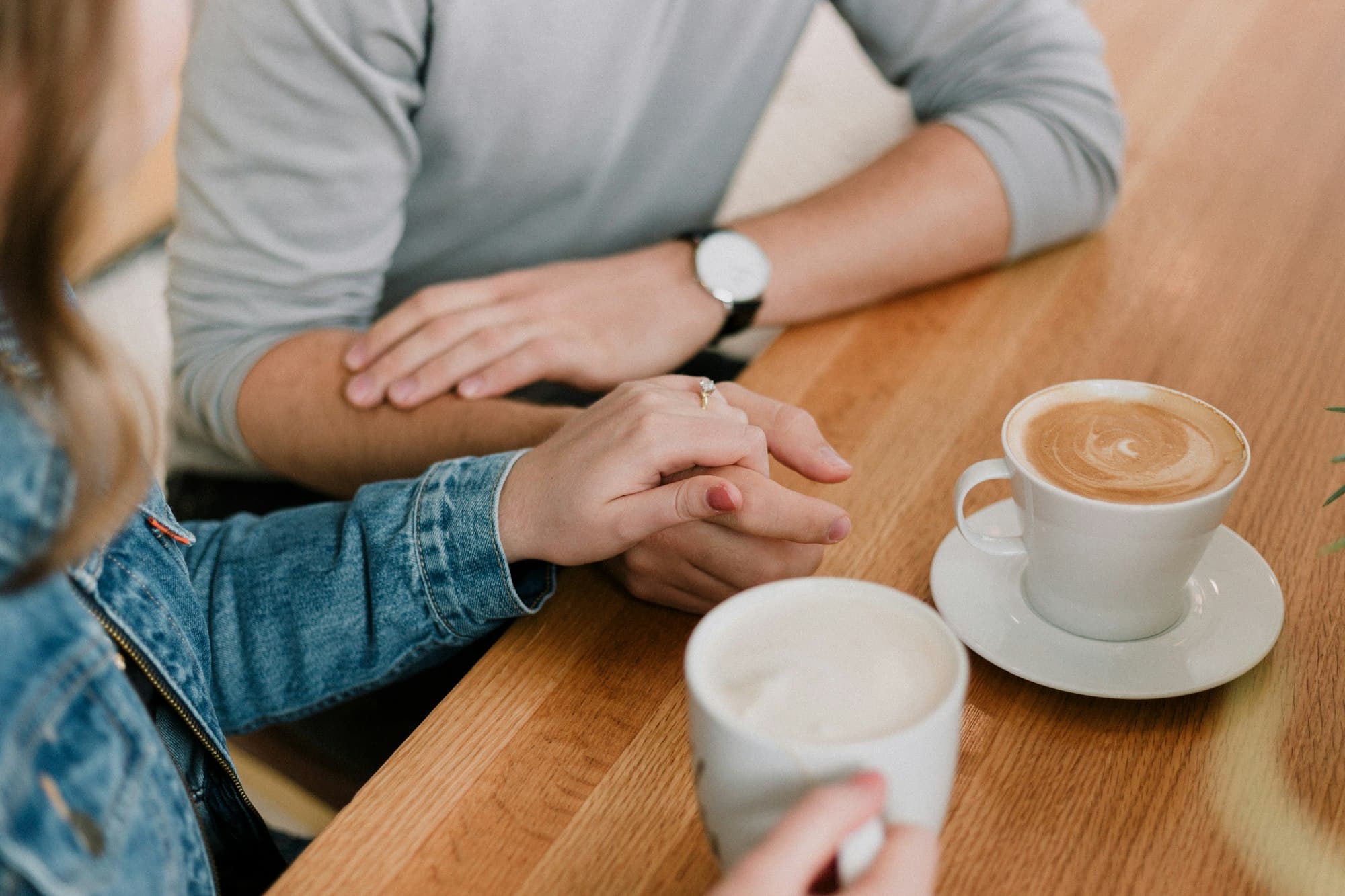Two people holding hands across a table, two cups of coffee between them