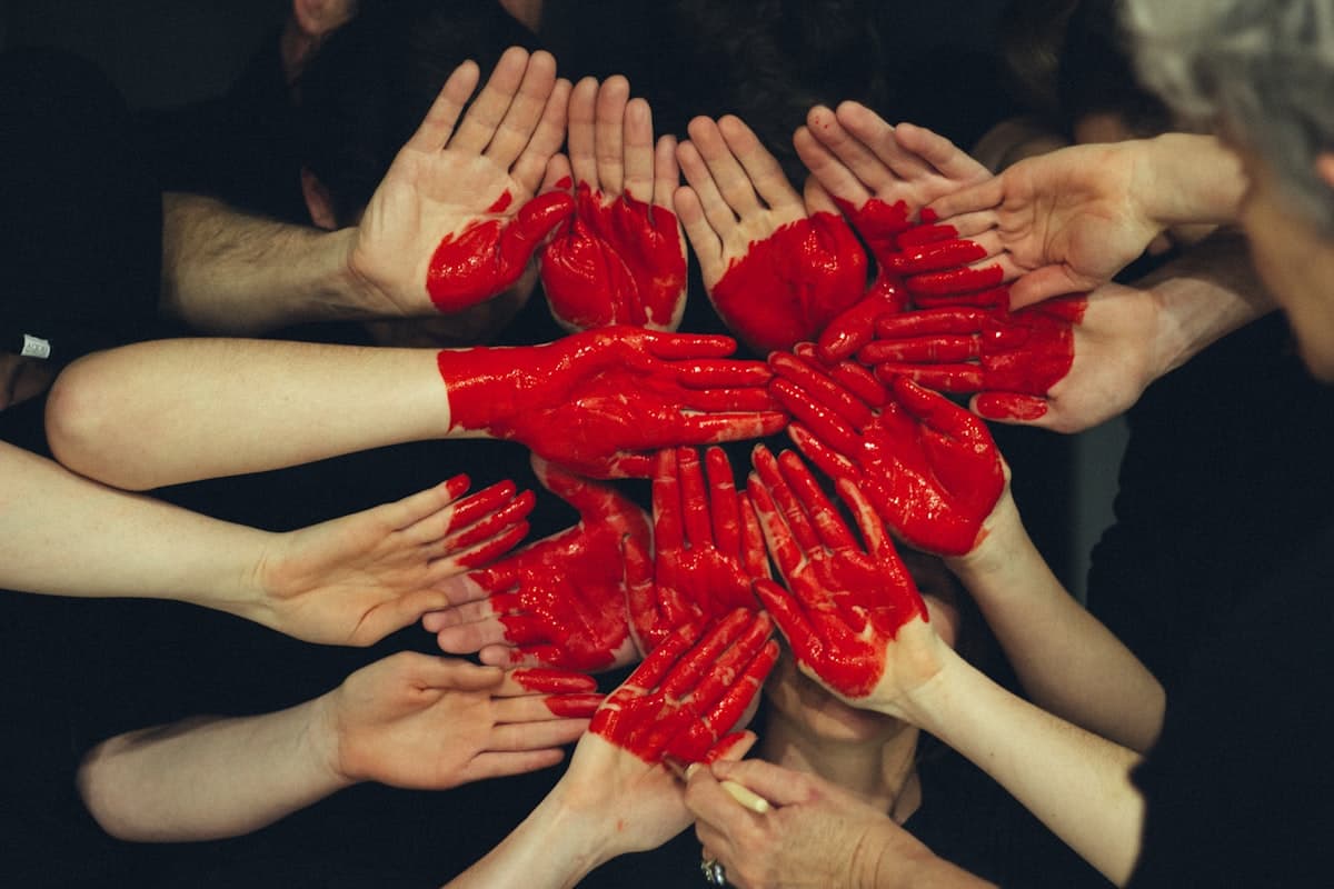 Many hands held out together, painted as one red heart