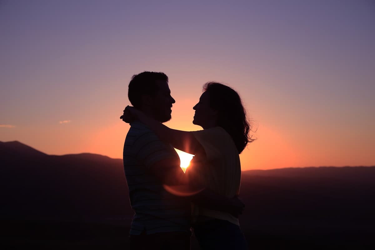 A couple embracing at sunset, silhouetted against the horizon